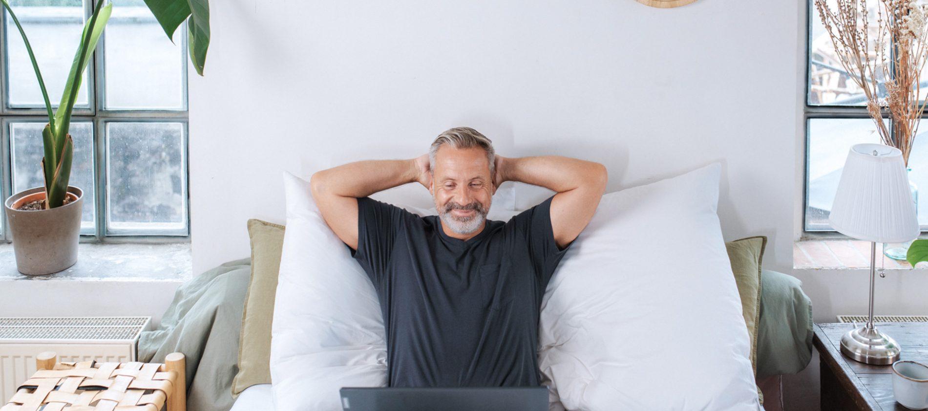 Mann arbeitet mit Laptop im Bett